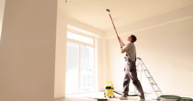 Işıkla dolu, parlak ve ferah bir odanın tavanını ustalıkla boyamak için bir silindir kullanan bir adam.