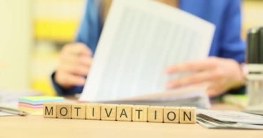 Çeşitli evrak işlerinin arasında motivasyonu ustalıkla heceleyen ve üretkenliği teşvik eden Scrabble harflerinin yakın plan çekimi.