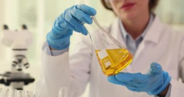 Kadın bilim adamı, içinde sarı sıvı bulunan matarayı eğiyor. Kadın profesyonel kimyager, petrolün akışkanlığını yavaş çekimde analiz etmek için uzmanlığını kullanır.