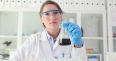 Kadın bilim adamı elinde koyu ham petrol içeren bir matara tutuyor. Araştırmacılar başarılı bir deneyi kutlamak için başparmak işareti gösteriyor