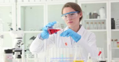 Genç kadın bilim adamı laboratuarda deney yapıyor. Araştırmacı yavaş çekim analizi için kırmızı sıvıyı test tüpüne boşaltıyor.