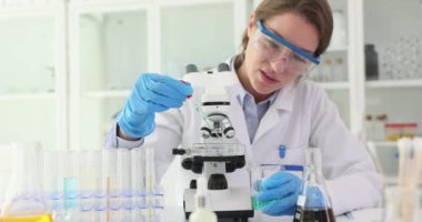 Kadın araştırmacılar pipeti kullanarak cam kaydırağa reaktör ekliyor. Bilim adamı, reaksiyonun özelliklerini mikroskop altında yavaş çekim incelemeye hazırlanıyor.