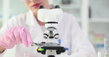 Laboratuvar önlüklü kadın kapsülü mikroskoba yerleştirmek için cımbız kullanıyor. Kadın bilim adamı klinikte ilaçların özelliklerini analiz ediyor.