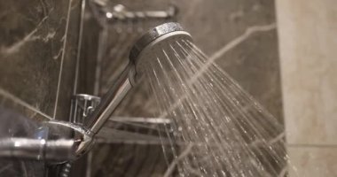 Mermer banyodaki parlak metalik duş başlığından çağlayan sular. Modern banyo alanındaki su akıntısı rahatlatıcı bir atmosfer yaratır.
