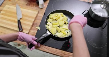 Steril eldivenli kadın spatula kullanarak patates kızartma tavasında karıştırıyor. Kadın aşçı mutfaktaki ocakta lezzetli yemekler pişiriyor.