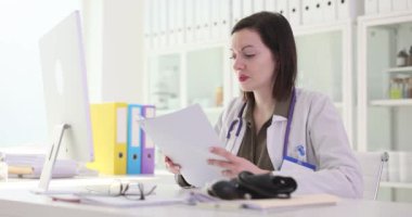 Kadın doktor klinikteki iş yerinde yapılan muayenenin tatsız bir sonucu olarak gazete okuyor. Üniformalı kadın doktor memnuniyetsizliği yansıtır.