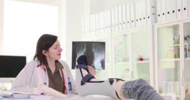 Kadın doktor, kırık bacağı olan kadın hastaya röntgen görüntüsü gösteriyor. Kadın hekim klinikte yaralanma tedavisi için gerekli adımları sıraladı