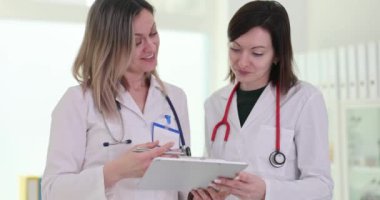 Kadın doktorlar test sonuçlarını klinikteki panoda incelerler. Gülümseyen kadın doktorlar, hastaların tedavi programını laboratuvarda ağır çekimde tartıştılar.