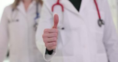 Kadın doktor, hastanede meslektaşının yanında baş parmak hareketi gösteriyor. Profesyonel sağlık görevlileri başarılı tedaviden memnuniyetlerini dile getirdiler