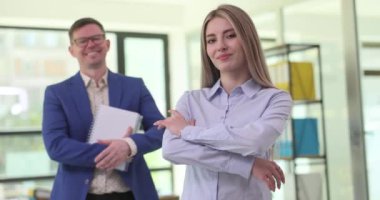 Pozitif iş adamları şirket ofisinde ağır çekimde gülümsüyor. Resmi giyinmiş kadın ve erkek, iş yerinde kendine güvendiğini gösteriyor.