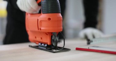 Eldivenli marangoz atölyede yapboz kullanarak masa için ahşap panel kesiyor. Erkek işçiler çalışma sürecine girerler. Ahşap ayrıntıları dikkatlice hazırlarlar.