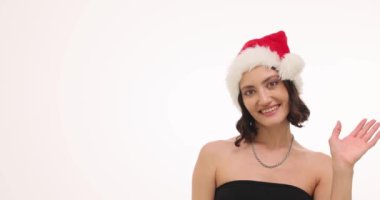 Neşeli bir kadın coşkulu ve neşeli bir Noel Baba şapkası takıp Noel ruhunu kucaklarken el sallıyor.