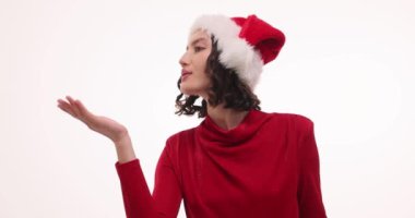 An elegant woman in a bright red dress and classic Santa hat, blowing a kiss for the joyful holiday season