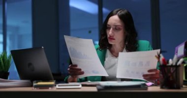 Modern bir ofiste, şık yeşil ceketli bir profesyonel titizlikle önemli belgeleri inceliyor.