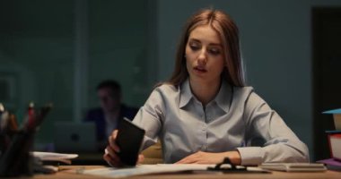 Yorgun kadın ofis katibi akıllı telefondan izliyor ve masaya uzanıyor. Çok çalışan bir bayan zehirli iş ortamının stresini hissediyor.