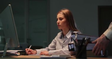 Çalışanlar evrak işleriyle çok meşguller. Dosyaları ofisteki masaların dışına atıyorlar. Sarışın kadın tezgahtar geç saatlere kadar şirket ortamında kalmayı reddediyor.