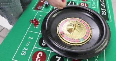 Krupiye, kumarhane çarkını çeviriyor ve oyun başlıyor. Kadın, elinde rakamlar ve rakamlarla kumar masasının yanında duran bir rulet masasına topu fırlatıyor.