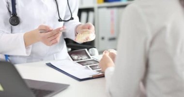 Kadın doktor, kadın hastayla görüştüğünde göğüs implantına işaret ediyor. Bayan doktor göğüs ultrasonu sonuçlarıyla masada oturuyor.