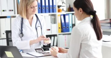 Sarışın kadın doktor kadın hastaya göğüs implantı seçenekleri gösteriyor. Laboratuvar önlüklü kadın doktor göğüs ultrasonu sonuçlarını klinikte tartışıyor.