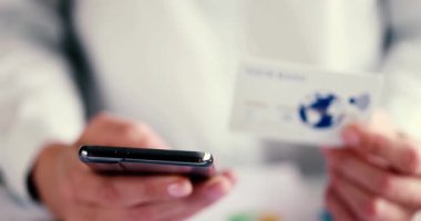 Bir kişi kredi kartını elinde tutarken zahmetsizce ödeme yapmak için akıllı telefonunu kullanır.