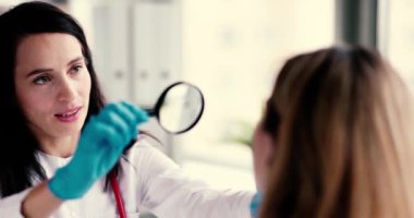 Bir dermatolog hastasının derisini yakından ve dikkatlice incelemek için bir büyüteç kullanır.