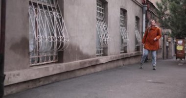 Kadın kaldırımda koşup kalabalığı tarıyor ve arkadaş arıyor. Kadın, işlek caddede kentsel mimari ve trafik akışını izliyor. Yavaş çekim