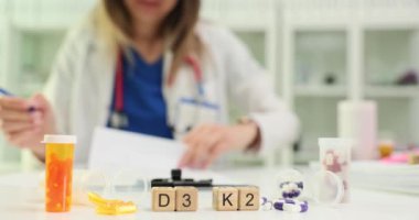 Küp ve ilaç şişelerinden gelen D3 ve K2 kelimeleri, klinikteki hastalara reçete yazan doktorlara karşı. Kadın doktor tavsiyeler üretiyor