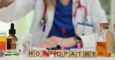 Doktorun klinikteki iş yerinde kapsül fırlatmasına karşı küplerden Homeopati kelimesi. Üniformalı kadın doktor yavaş çekimde alternatif tedavi seçenekleri sunuyor