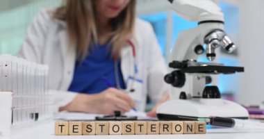 Test örneklerini mikroskop ile inceleyen tıbbi araştırmacı bilim adamına karşı kelime Testosteronu. Kadın doktor biyolojik verileri yavaş çekimde analiz ediyor.