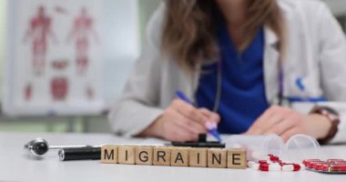 Migren için kullanılan tıbbi terim tahta küpler ve masa başında yazan doktorlardan geliyor. Kadın terapist, baş ağrısı olan hastaya ilaç yazıyor.