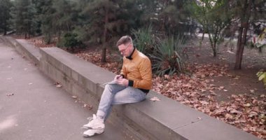 Yaratıcı erkek profesyonel belgeler not defterinde ilham verici düşünceler alçak duvarda oturuyor. Gözlüklü sakin adam sonbahar parkında dinlenen notlar yazıyor.