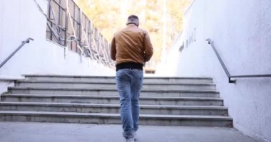 Deri ceketli bir erkek yaya ve kot pantolon dikiz aynasından beton merdivenlere tırmanıyor. Adam şehir caddesinde ilerlerken, sonbahar günü yavaş çekimde kağıt kaybediyor.