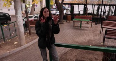 Siyah ceketli ve kot pantolonlu genç bir kadın sokak kafesinin yanında ruj sürüyor. Güzel bayan makyajını şehir ortamında yavaş çekimde ayarlıyor.