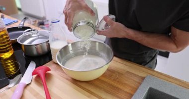 Profesyonel şef cam kavanozdan tezgahtaki metal kaseye un döker. Adam mutfakta ev yapımı kek pişirmek için malzemeleri yavaş çekimde hazırlıyor.