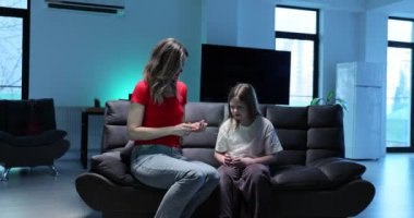 Anne, oturma odasındaki koltukta oturan bir bardak su tutan kızına ilaç veriyor. Kadın, ağır çekimde acı çeken çocuğa bakıyor.