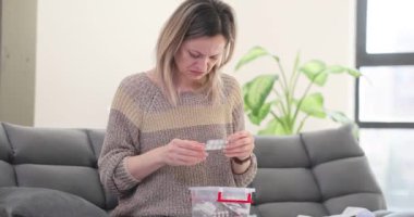 Kadın evdeki kanepede oturan şeffaf kutuda hap arıyor. Kadın, reçeteli ilaç bulmaya çalışırken acı veren semptomlar yaşıyor.