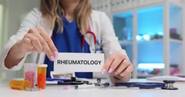 Kadın doktor hastanede kağıt üzerinde kelime romatolojisi gösteriyor. Kemiklerde iltihap, eklemlerde kaslar ve iç organlarda tedavi
