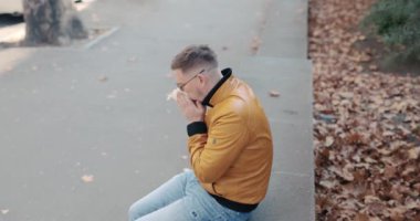 Şehir caddesinde oturan uzun elbiseli adam burnunu siliyor. Deri ceketli adam sabah yürüyüşü sırasında kendini kötü hissediyor.