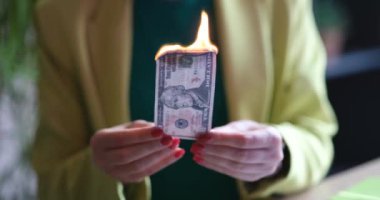 Bir kişi, finansal atıkları ve devam eden toplumsal zorlukları simgeleyen yanan bir banknotu havada tutar.