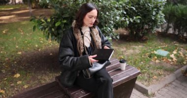 Genç bir kadın ahşap parktaki bankta oturur ve defterini açar. Kadın, düzenli yazılmış notlar ve çizimlerle dolu günlüğü açıyor. Yavaş çekim