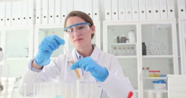 Laboratuvar çalışanı test tüpünde sıvı karıştırmak için cam çubuk kullanır. Gözlüklü kadın bilim adamı test tüpünün içindekileri karıştırıyor. Yavaş çekim