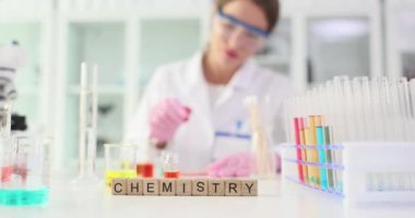 Tahta küplerle süslenmiş bir masa. Kelime kimyasalı oluşturuyorlar. Odaklanmış kadın kimyager deney tüplerine reaktör eklemek için pipet kullanır. Yavaş çekim