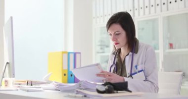Kadın doktor bir yığın hastanın tıbbi kayıtlarını inceliyor. Doktor, gerekli bilgileri saptamak için hastaların tıbbi geçmişini okur. Yavaş çekim