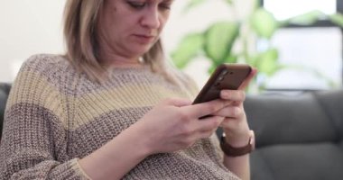 Kadın rahat bir koltukta oturuyor ve sosyal medyada mesajlar okuyor. Konsantre dişi önemli mesajlara cevap vermek için akıllı telefonu kullanır. Yavaş çekim