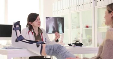Doktor, kırığın tam yerini röntgen görüntüsü kullanarak gösteriyor. Kadın doktor, kadın hastaya tedavi planının etkinliğinden bahsediyor. Yavaş çekim