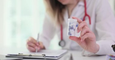 Kadın doktor, klinikte reçete yazan haplarla dolu şişeyi gösteriyor. Steteskoplu kadın doktor randevuda hasta için etkili bir tedavi hazırlıyor