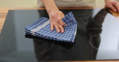 Kadın dikkatli bir şekilde elektrikli sobayı kareli bezle temizliyor. Ev hanımı, mutfağı temizleme sürecine girer.
