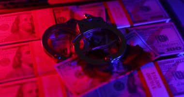 Polis fenerleriyle aydınlatılmış bir valizin içindeki bir yığın banknotun üstüne kelepçelenmiş. Mali suç kavramı ve hukuki sonuçlar
