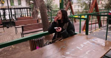 Kadın çocuk parkının yanındaki piknik masasında kek yiyor. Genç dişiler, boş şehir parkında sıcak bir sonbahar gününde zevkten dört köşe olurlar.