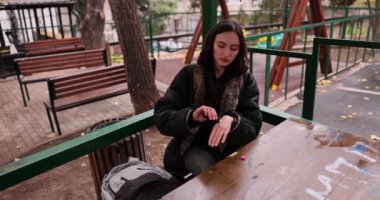 Genç bir kadın parkta piknik masasında otururken nemlendirici el kremi sürüyor. Dişi, yumuşak cildi değişen mevsimsel koşullardan korur. Yavaş çekim.